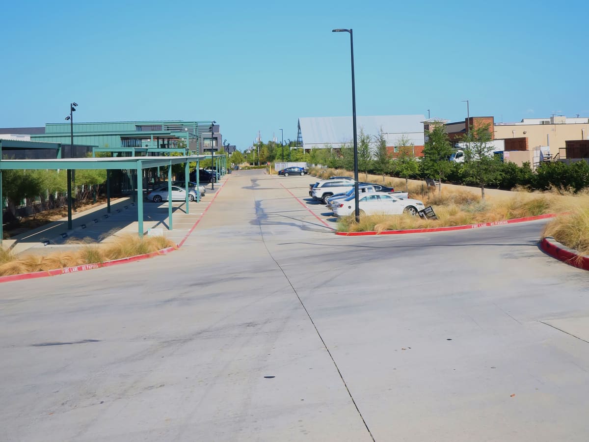 The road in from K Avenue, looking east: covered office parking on the left, open public parking down the right side.