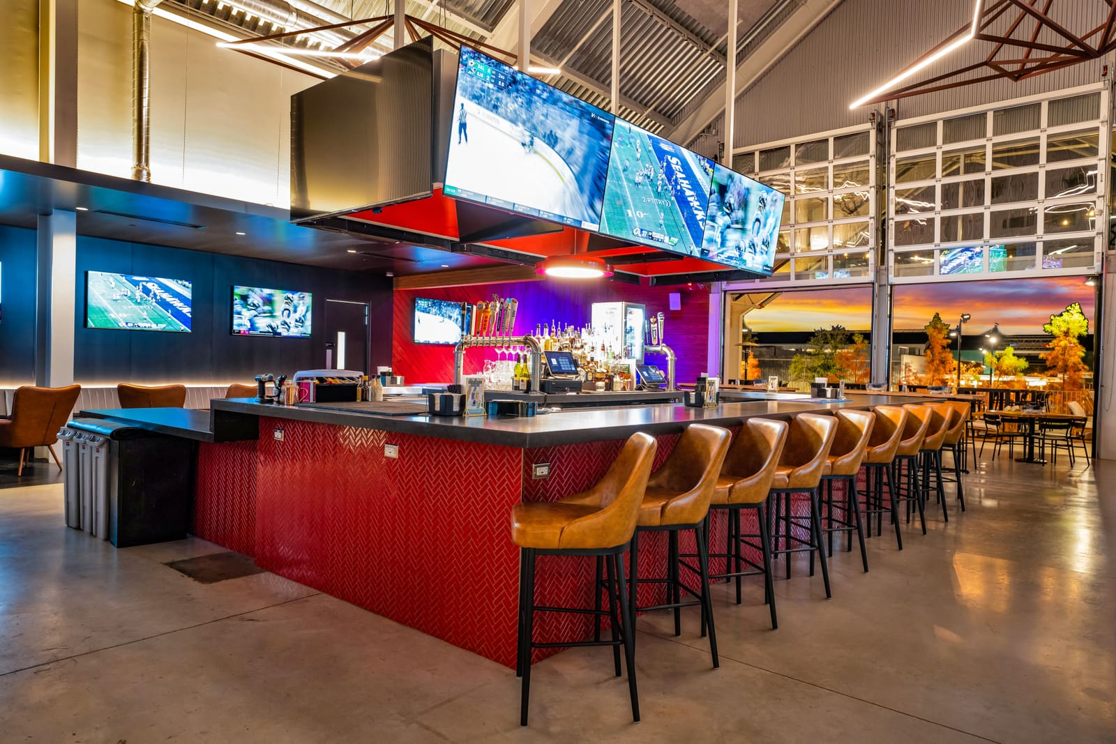 The main bar at Assembly Icehouse: the red bar front, tan stools along it and the lighting rig overhead