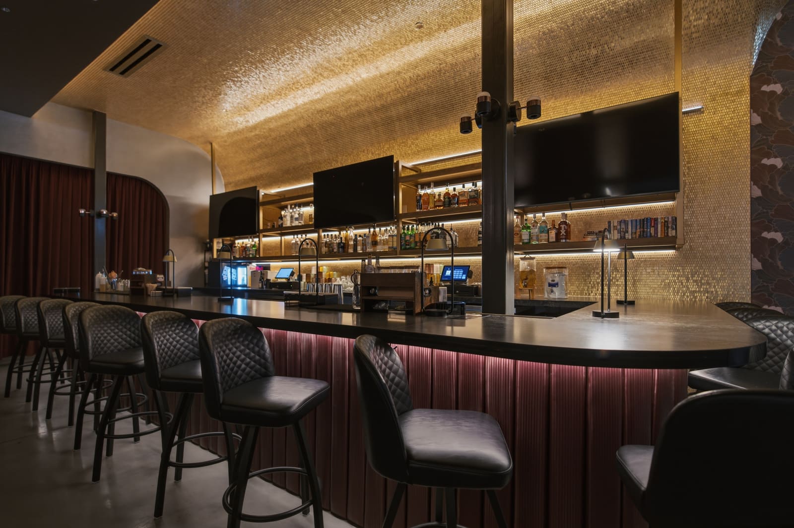 Along the lounge bar: quilted stools, the gold-tiled ceiling above, bottles and screens on the back bar
