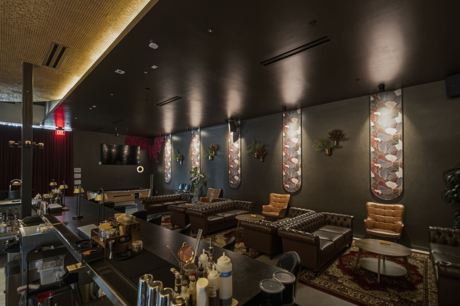The length of the lounge: seating along the botanical wall panels, the service bar in the foreground, a screen at the far end