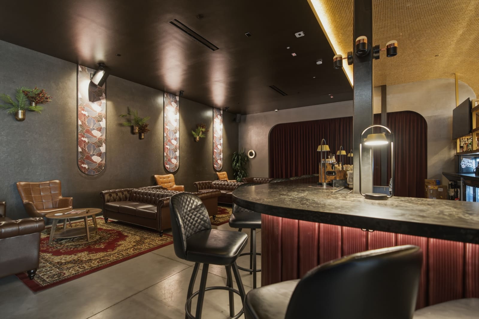 Chesterfield couches and tan leather armchairs on a patterned rug, the curved bar edge at the right