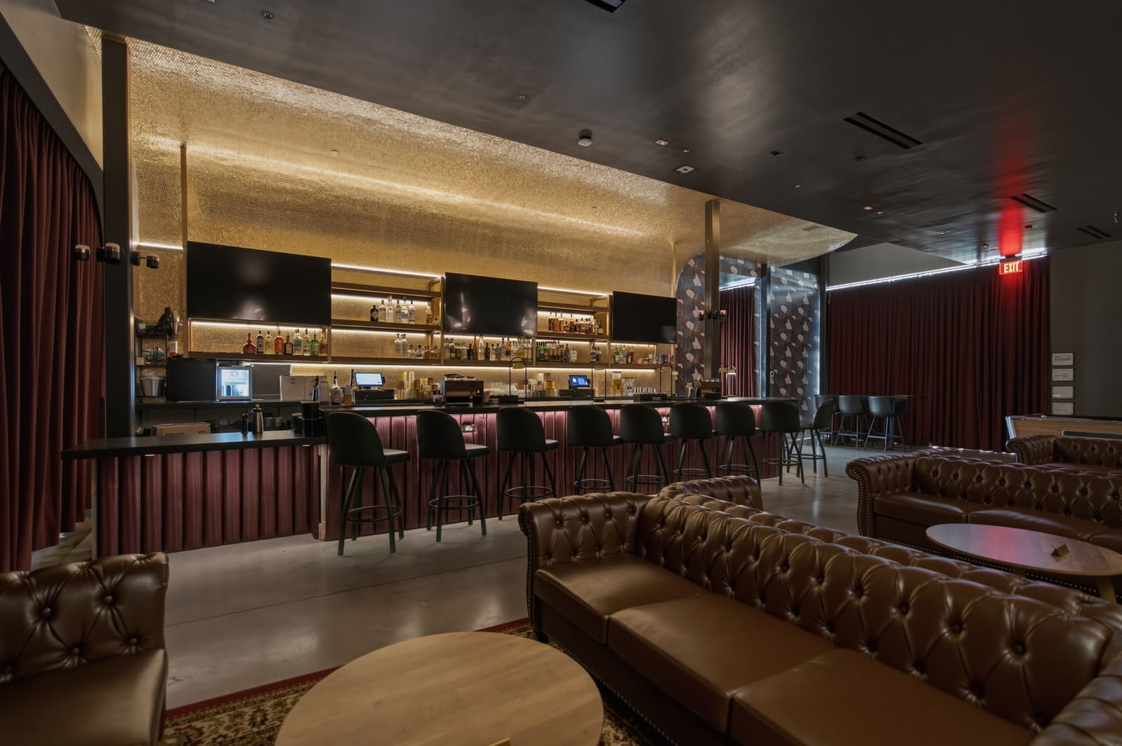 The lounge set for a party: leather chesterfields and round tables in the foreground, the lit bar and its stools behind