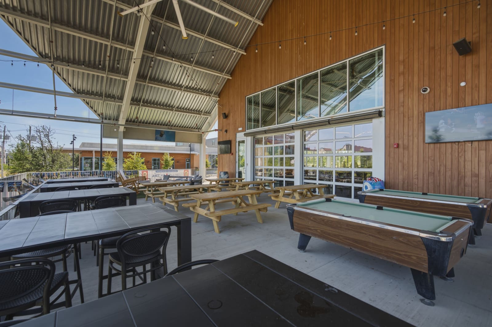 Two pool tables under the covered patio roof, picnic tables beyond them