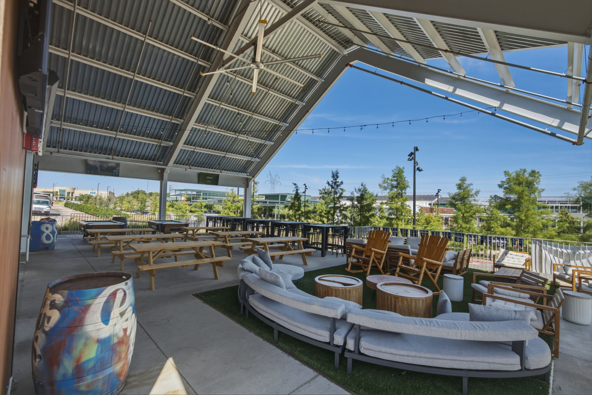 The covered patio, empty: a curved couch on the turf, picnic tables behind it, trees and sky past the rail